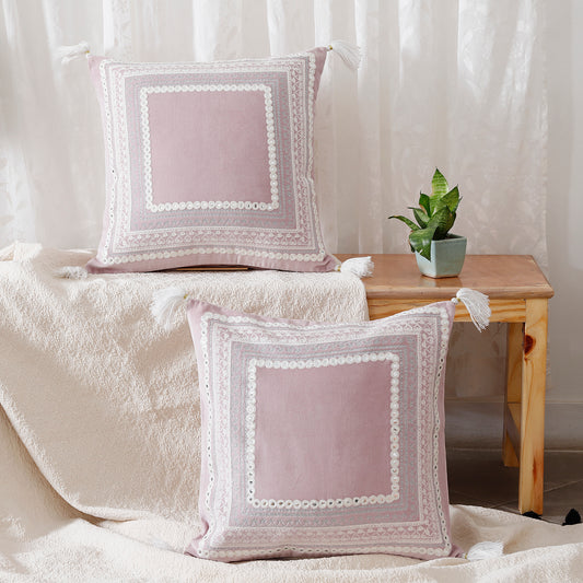 Two pink pillows with white lace on them, sitting on a wooden table next to a plant.