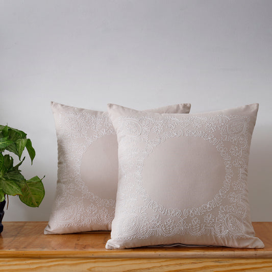 Two beige cotton throw pillows with delicate embroidery.